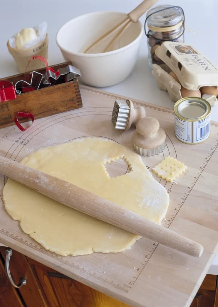 Masa de galletas estirada sobre una tabla, con rodillo y cortadores