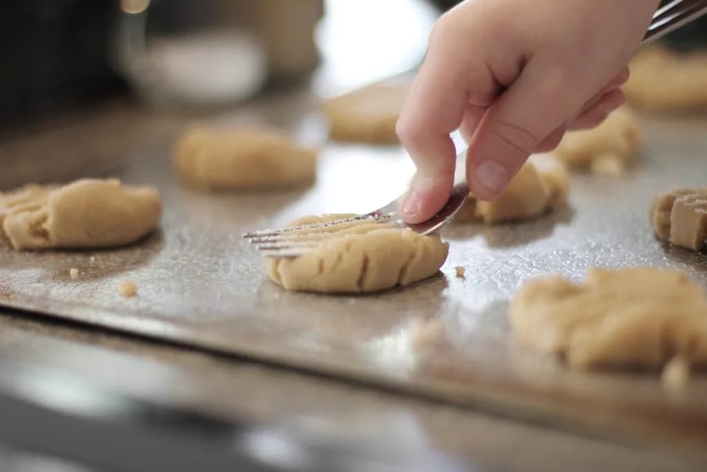 Una mano marca con un tenedor las galletas colocadas en la bandeja del horno
